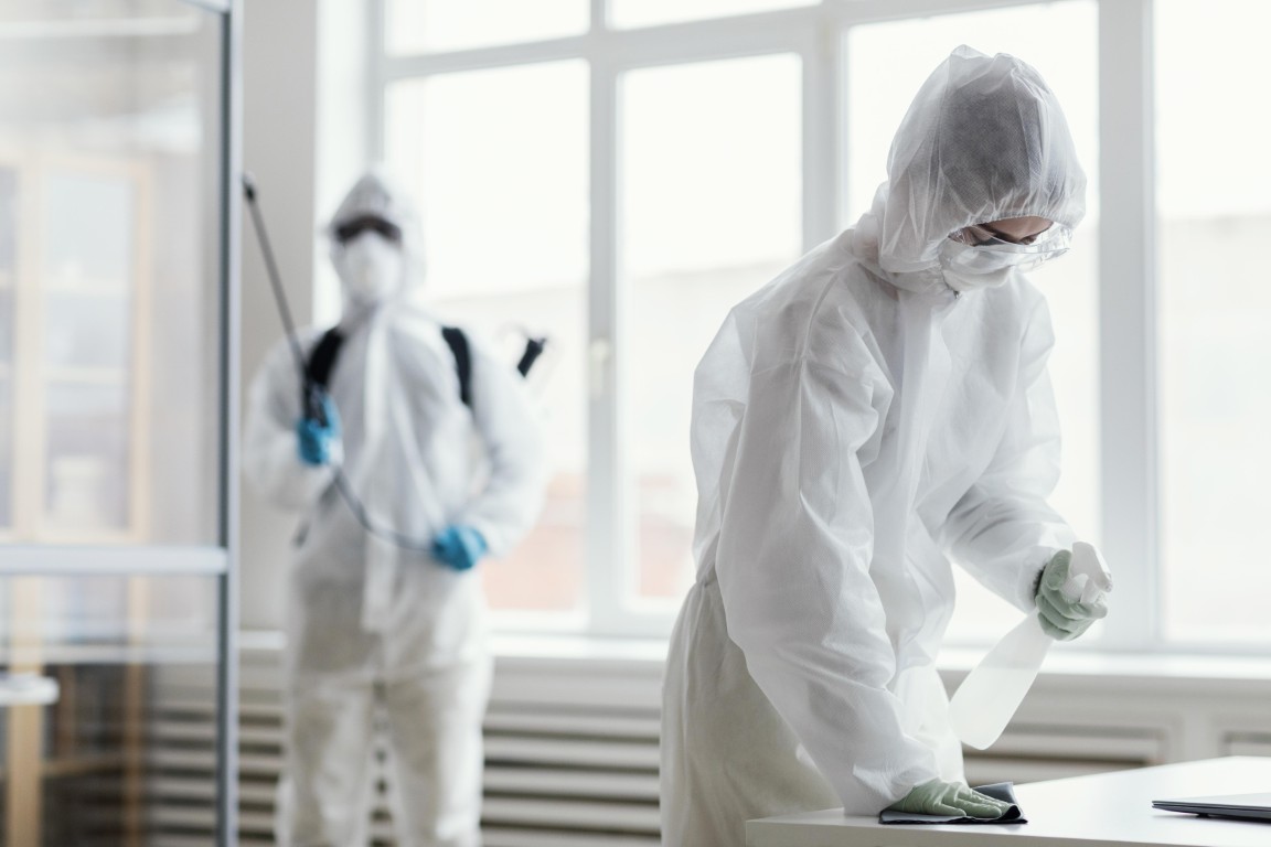 Двое специалистов в белых защитных костюмах проводят уборку и дезинфекцию