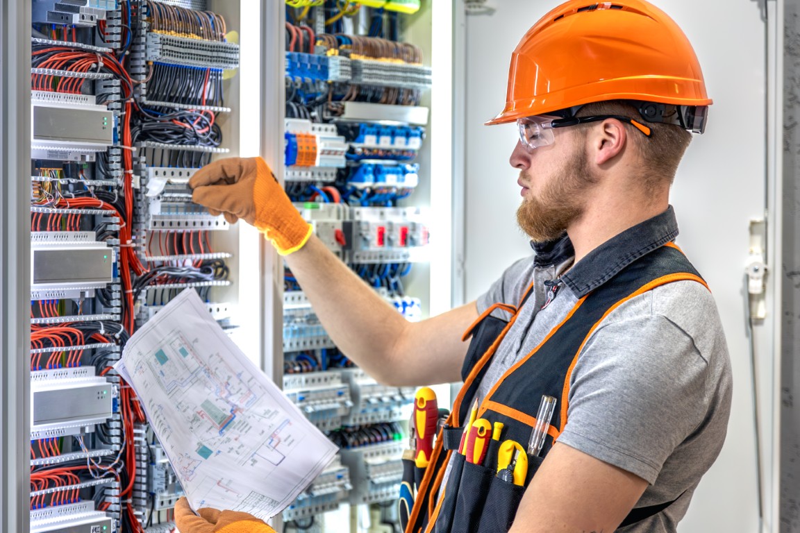 Male electrician working in electrical panel. Male electrician in overalls.