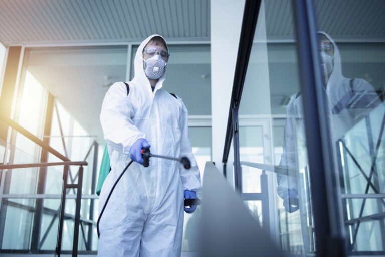 Специалист в защитном костюме проводит дезинфекцию помещения